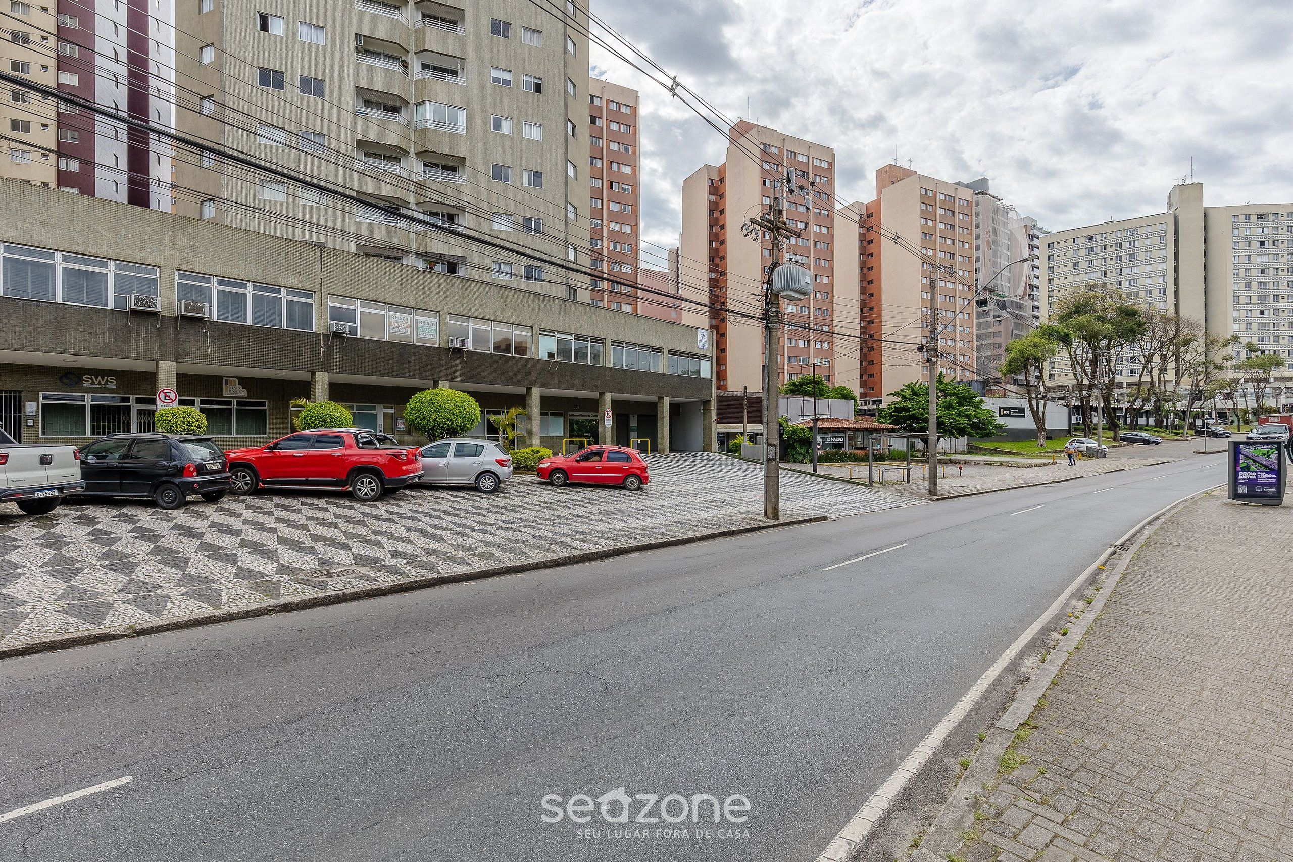 Ein Parkplatz mit mehreren Autos, ein mehrstöckiges Gebäude und ein Fußweg.