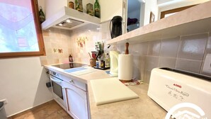 A kitchen with a stove, oven, and countertop. There are various kitchen items and a window. - La Cave de Jean - GARDIE (GARDIE)