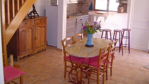 Una cocina con comedor, armarios de madera, un refrigerador y un florero con flores sobre la mesa.