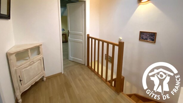 A hallway with a wooden staircase, a white door leading to another room, and a small cabinet. - La Cave de Jean - GARDIE (GARDIE)