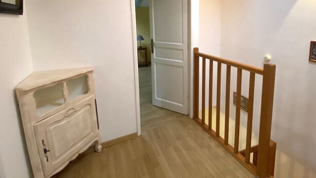 Un pasillo con una escalera de madera, una puerta blanca que da a otra habitación y un armario pequeño.