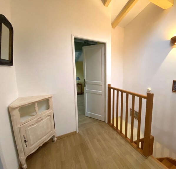 A hallway with a wooden staircase, a white door leading to another room, and a small cabinet.