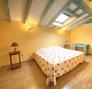 A bedroom with a bed, a small table, a lamp, a wardrobe, and a skylight.