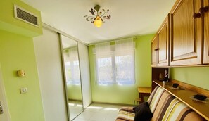A living room with a striped sofa, a small table, and a kitchen area with wooden cabinets.