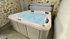 A hot tub with a stone wall backdrop, a shower area, and a tiled floor. - Le Vieux Puits - CAUNES MINERVOIS (CAUNES MINERVOIS)
