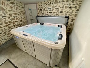 Un bain à remous avec un mur en pierres en arrière-plan, un espace douche et un sol carrelé.