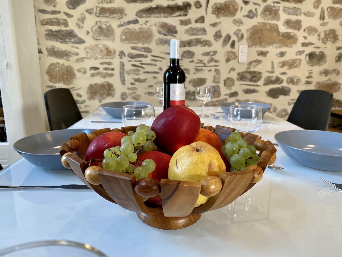 A wooden fruit bowl on a table with a stone wall background.