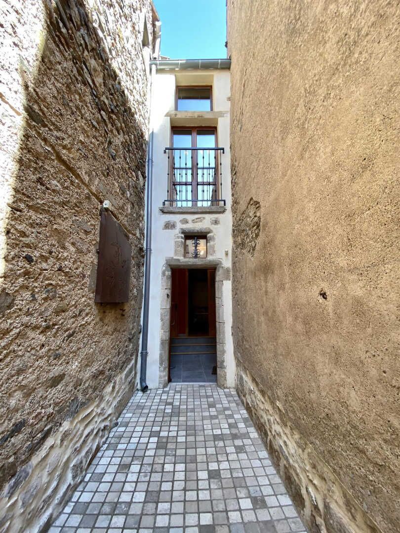 A narrow alleyway with a tiled floor, flanked by stone walls, leading to a building with a balcony.