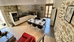 A modern kitchen with stone walls, a dining area with a red sofa, and a staircase leading to another level. - Le Vieux Puits - CAUNES MINERVOIS (CAUNES MINERVOIS)