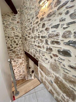 Un escalier étroit, avec des murs en pierre et une main courante en bois.