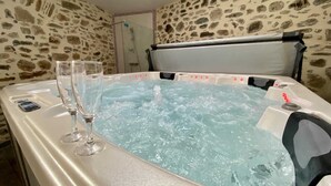 A hot tub with two glasses on the side, set against a stone wall background. - Le Vieux Puits - CAUNES MINERVOIS (CAUNES MINERVOIS)