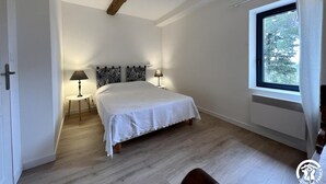 Ein Schlafzimmer mit einem großen Bett, zwei Nachttischlampen, einem Fenster mit Blick auf Bäume und einem Holzbalken an der Decke.