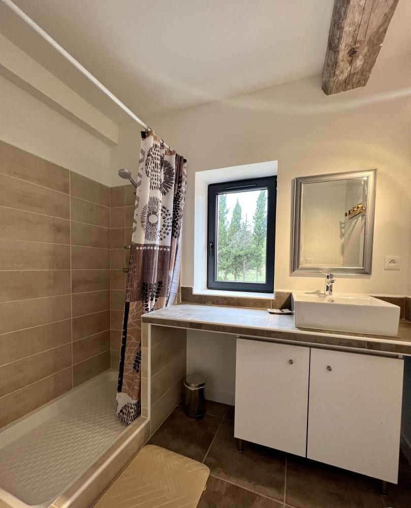 A bathroom with a shower, a window, a sink, and cabinets.