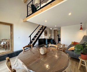 Una sala moderna con una mesa redonda, un sofá, una escalera y una cocina al fondo.