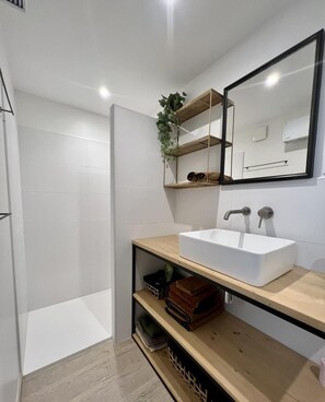 Un baño moderno con un lavabo blanco, repisas de madera y un espejo.