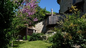 Un bâtiment rustique en pierre, doté d’une porte en bois et d’une petite structure en bois en arrière-plan.