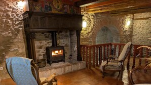 Une pièce aux murs de pierre, avec un poêle à bois, une chaise en bois et une table.
