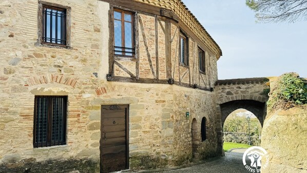 A stone building with a wooden door, windows, and an archway. - Gîte de la Porte d'Aval (ISSEL)