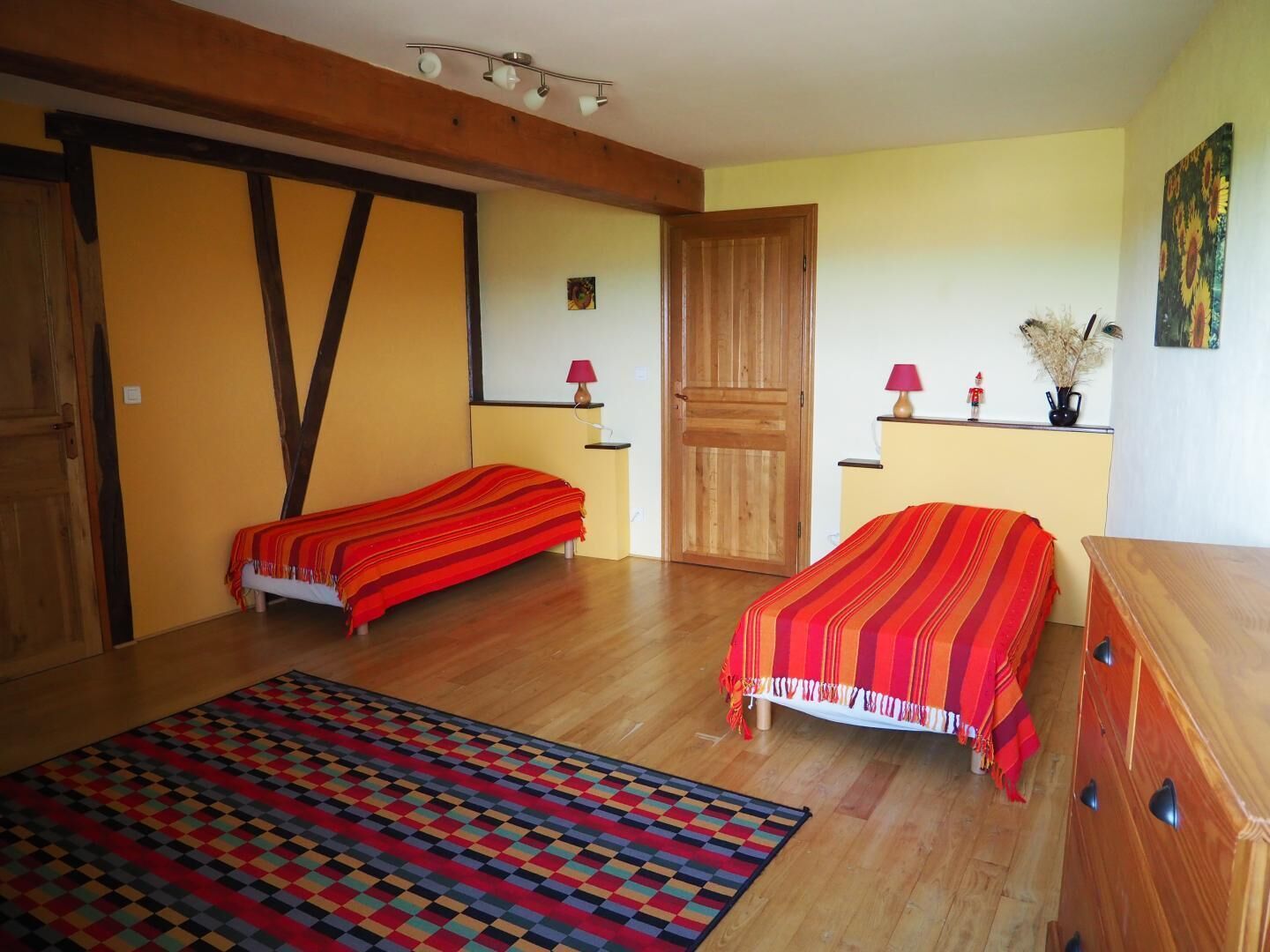 A room with two beds, a wooden dresser, a patterned rug, and a door.