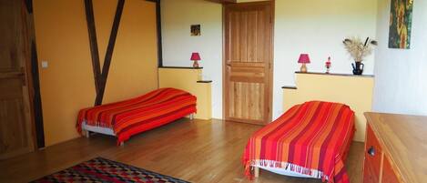 A room with two beds, a wooden dresser, a patterned rug, and a door.
