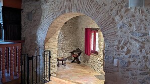 Une pièce aux murs de pierre, avec un banc en bois, une petite table et un rideau rouge.