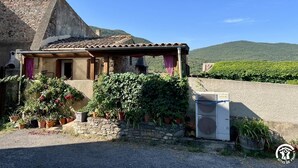 Une maison de campagne en pierre, avec un toit en tuiles, une véranda et un jardin agrémenté de plantes en pot.