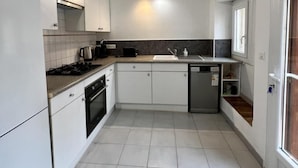 Une cuisine moderne avec des meubles blancs, une cuisinière à gaz, un lave-vaisselle et une petite fenêtre.