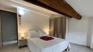 Une chambre à coucher avec un lit, des tables de chevet, une couverture rouge, une poutre en bois au plafond et un luminaire.