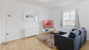Un salon moderne avec un canapé, un téléviseur, un miroir et une fenêtre avec des rideaux.
