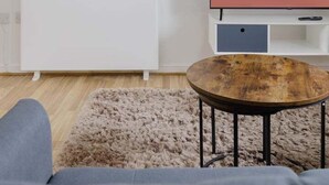 Un salon moderne avec une console blanche, une table basse ronde en bois, un tapis beige moelleux et un téléviseur à écran plat affichant le message « PRÊT POUR LES INVITÉS ».