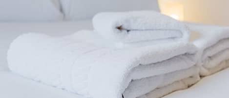 A neatly made bed with white linens and folded towels.