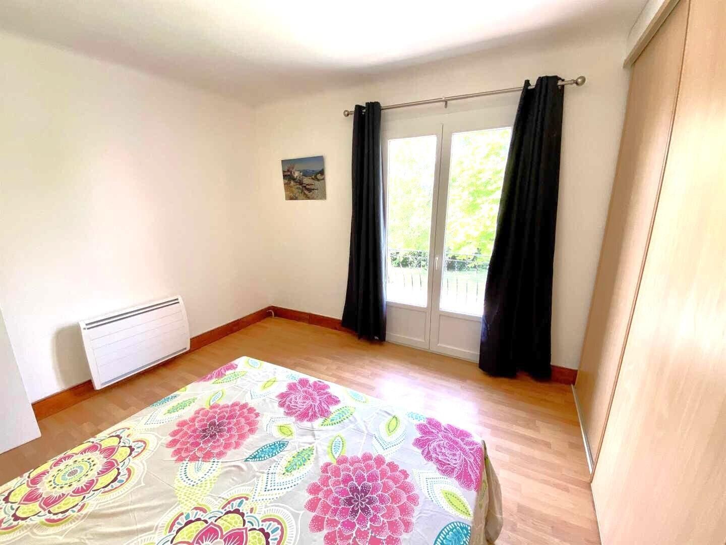 A bedroom with a bed, a radiator, a window with curtains, and a small painting on the wall.