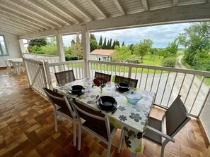 A covered patio with a table set for dining, surrounded by chairs, overlooking a scenic landscape.