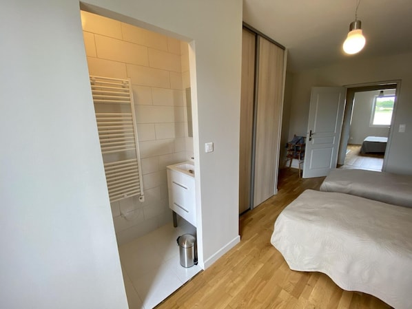 A bedroom with a wooden floor, a white bed, a radiator, and a small trash bin.