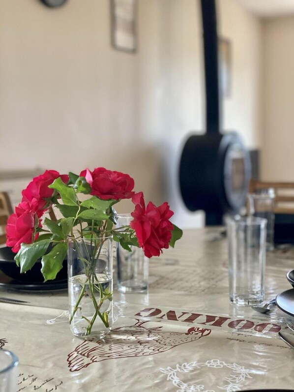 A dining table with a clear glass vase containing red flowers, a decorative table runner, and several clear glasses.