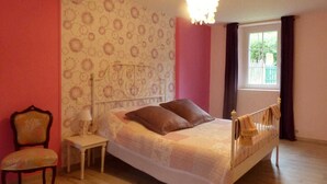 Quarto com cama, cadeira, mesa de cabeceira e janela com cortinas.