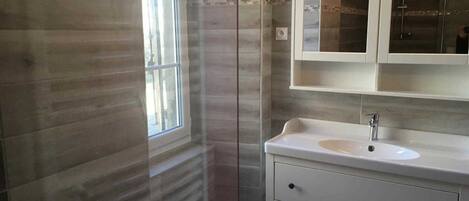 A bathroom with a large window, a sink with a mirror above it, and a shower area.