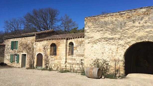 Um edifício rústico de pedra com janelas em arco e um barril em primeiro plano.