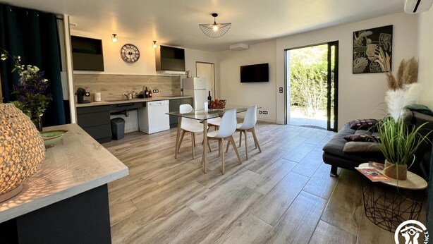 Un appartement moderne comprenant une cuisine, un coin repas et un salon. Il est doté d’une grande fenêtre, d’un téléviseur à écran plat et d’une plante décorative.