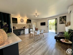 A modern apartment with a kitchen, dining area, and living room. It features a large window, a flat-screen TV, and a decorative plant. - In the shade of the Olive Tree (MIREPEISSET)
