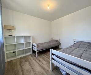 A bedroom with two single beds, a white shelf unit, and a lamp.