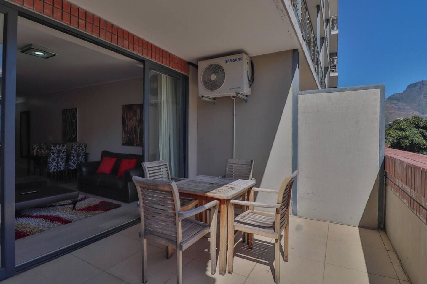 An outdoor balcony with a table and chairs, a Samsung air conditioning unit, and a view of the mountains.