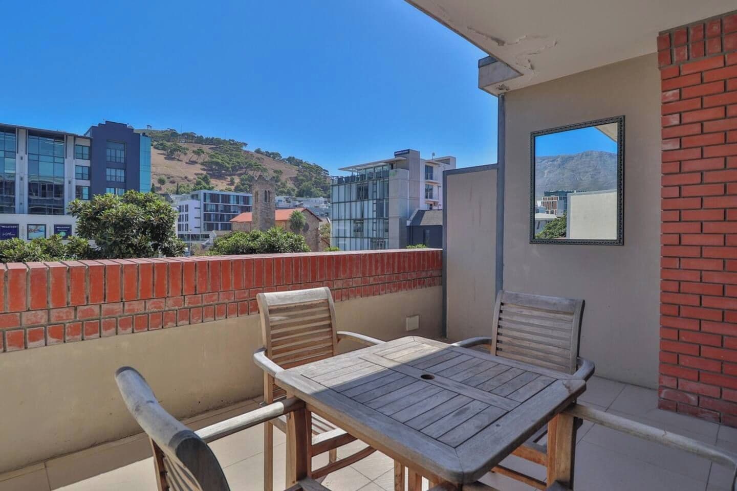 Een balkon met een tafel en stoelen, een bakstenen muur en uitzicht op gebouwen en heuvels.