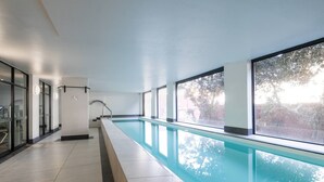 A long indoor swimming pool with clear glass walls and a view of trees outside. - De Waterkant 1br|pool, Gym & balcony views by ctha (Cape Town)