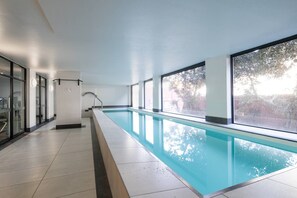 Una lunga piscina interna con pareti di vetro trasparente e vista su alberi all'esterno.