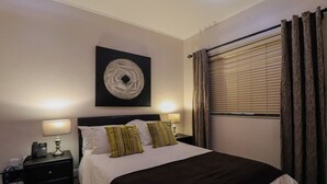 A hotel room with a bed, two bedside tables, a wall-mounted artwork, and a window with curtains. - De Waterkant 1br|pool, Gym & balcony views by ctha (Cape Town)