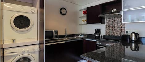 A compact kitchen with a washing machine, microwave, sink, and a clock on the wall.