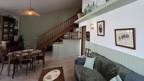 Un espace repas avec un escalier en bois, un coin cuisine et un salon avec un canapé et des coussins.