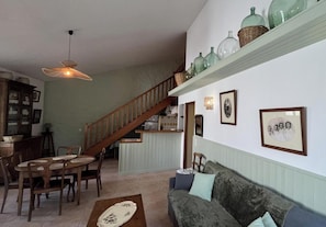 Un espace repas avec un escalier en bois, un coin cuisine et un salon avec un canapé et des coussins.