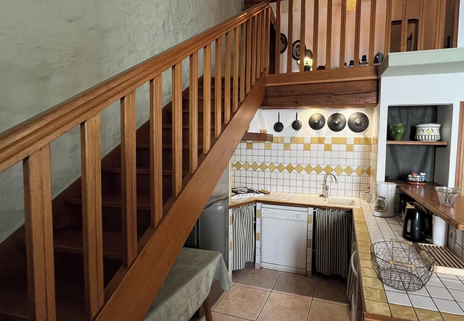 Une cuisine avec un escalier en bois, un plan de travail recouvert de carreaux, un évier et une machine à café.